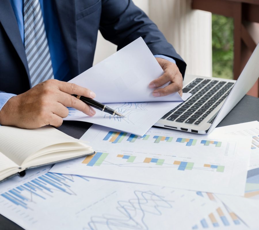 businessman-hand-holding-pen-analysis-the-graph-with-laptop-at-the-home-office.jpg